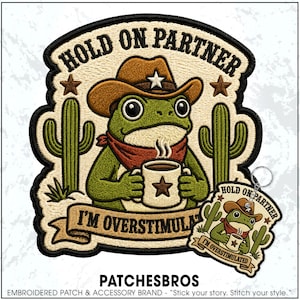 May include: An embroidered patch and matching keychain featuring a green frog wearing a brown cowboy hat and red bandana, holding a steaming mug with a star icon. The text reads HOLD ON PARTNER and I'M OVERSTIMULATED, framed by two green cacti.