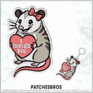 May include: Embroidered patch and keychain featuring a cartoon opossum holding a heart. The heart is pink with the words "I tolerate you". The opossum has a pink bow and is gray, white, and pink.