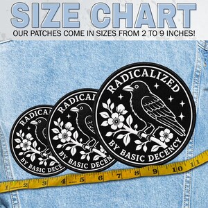 May include: Three circular black embroidered patches featuring a white crow perched on a flowering branch. The text reads RADICALIZED BY BASIC DECENCY. A yellow measuring tape shows sizes ranging from 2 to 9 inches on a light blue denim fabric background.