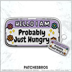 May include: Embroidered patch and keychain with the text "HELLO I AM Probably Just Hungry." The patch is rectangular with a purple background, white border, and floral accents. The keychain has a similar design.