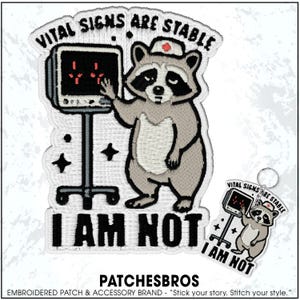 May include: Embroidered patch featuring a raccoon wearing a nurse's cap, standing next to a medical monitor. The text "VITAL SIGNS ARE STABLE" arches above the raccoon, with "I AM NOT" below. A smaller keychain with the same design is also visible.