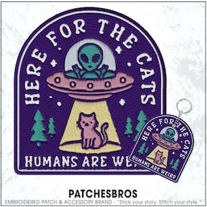 May include: Embroidered patch and keychain set with a purple background. The patch features a UFO with an alien, a cat, and the text "HERE FOR THE CATS, HUMANS ARE WEIRD." The keychain has the same design.