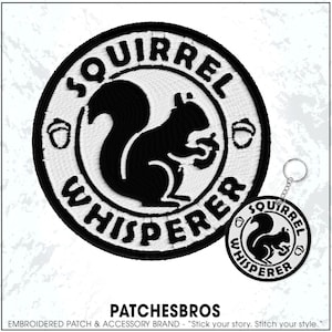 May include: Embroidered patch and keychain featuring a black squirrel holding a nut, surrounded by the words "Squirrel Whisperer" in a circular design. The patch and keychain are white with black text and details.