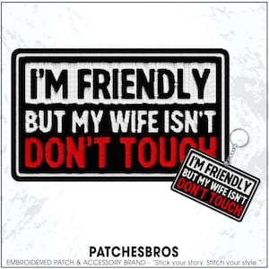 May include: Black and white embroidered patch with the text "I'M FRIENDLY BUT MY WIFE ISN'T DON'T TOUCH". A matching keychain is attached. The patch and keychain have a black border and white text with red text for "DON'T TOUCH".