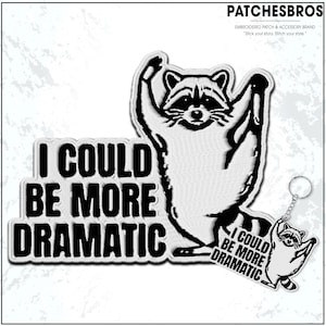 May include: Embroidered patch and keychain set featuring a raccoon with arms raised. The patch and keychain both have the text "I COULD BE MORE DRAMATIC" in black block letters. The brand name "PATCHESBROS" is at the top.
