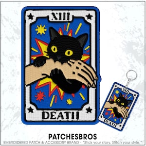 May include: Embroidered patch and keychain set featuring a black cat biting a skeletal hand, set against a blue background with yellow and red accents. The patch and keychain are in the shape of a tarot card, with the word "DEATH" at the bottom.