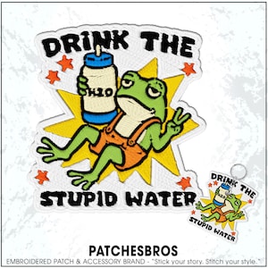 May include: An embroidered patch and matching keychain featuring a green frog wearing orange overalls, holding a blue and white water bottle labeled H2O, set against a yellow starburst with orange stars and the text DRINK THE STUPID WATER.