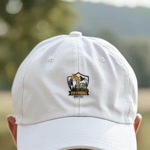 May include: A white baseball cap featuring a central graphic of a yellow excavator inside a shield-shaped emblem. The design includes mountain silhouettes and pine trees, with the text ANYNAME and ANYTEXT printed in black on a yellow banner.