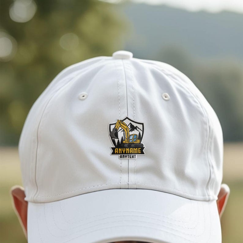 May include: A white baseball cap featuring a central graphic of a yellow excavator inside a shield-shaped emblem. The design includes mountain silhouettes and pine trees, with the text ANYNAME and ANYTEXT printed in black on a yellow banner.