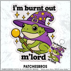 May include: An embroidered patch and matching keychain featuring a green frog wearing a purple wizard hat with yellow stars and a purple cape. The frog holds a yellow wand. The text reads i'm burnt out m'lord in black lettering.