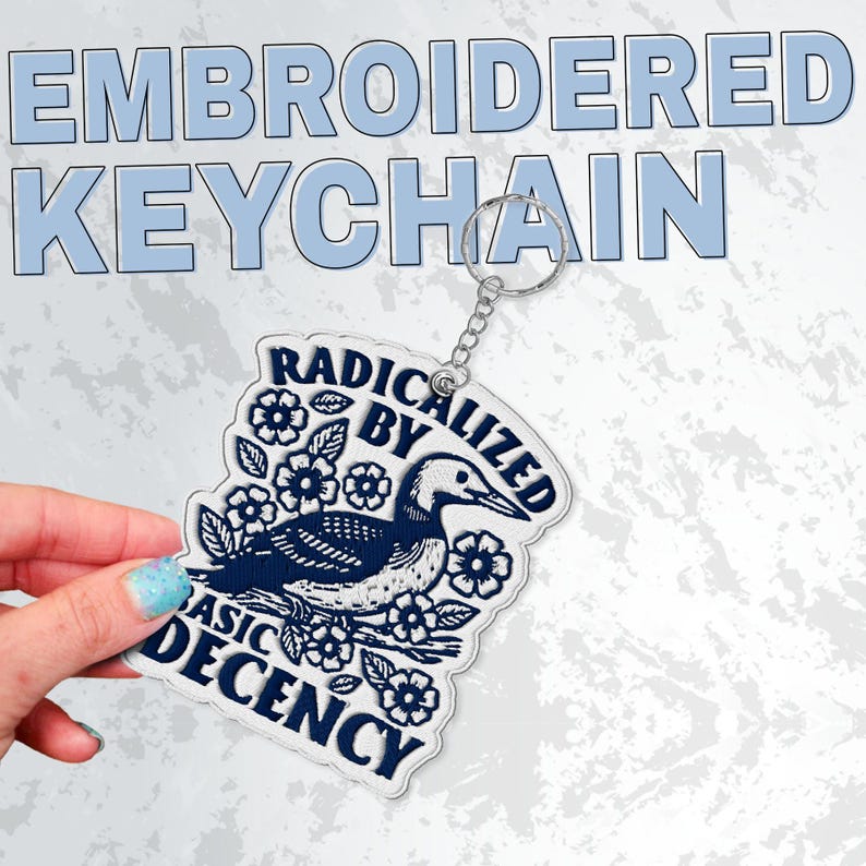 May include: Embroidered keychain with a loon design, surrounded by flowers and leaves, and the text "RADICALIZED BY BASIC DECENCY". The keychain is white with navy blue embroidery and a silver chain.