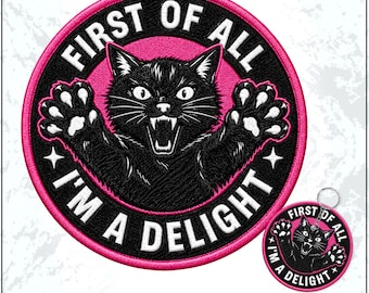 May include: A circular embroidered patch and a matching keyring featuring a black cat with bared teeth and raised paws. The design includes a bright pink border and the white text FIRST OF ALL I'M A DELIGHT set against a black background.