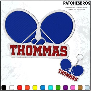 May include: Embroidered patch and keychain set featuring a blue and white design with the name "THOMMAS" in red. The patch has a unique shape, and the keychain mirrors the patch design. The brand name "PATCHESBROS" is also visible.