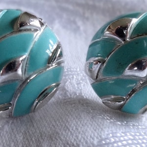 May include: A pair of turquoise and silver earrings with a geometric design. The earrings are round and have a textured surface.