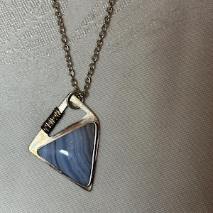 May include: A silver chain necklace with a triangular pendant featuring a blue agate stone set in a silver frame.
