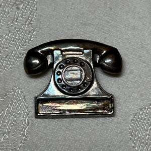 Serling silver brooch that resembles a retro desk telephone, with a space for a name