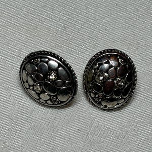 May include: A pair of silver tone earrings with a textured pebble design and clear rhinestones.