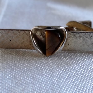 May include: Silver tie clip with a heart-shaped tiger's eye stone.