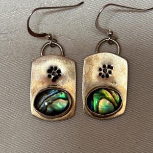 May include: A pair of silver earrings with a green and blue abalone shell inlay and a silver flower design.