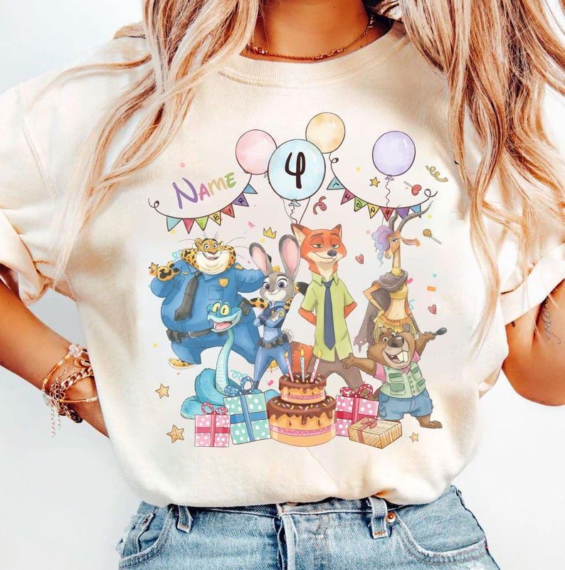 May include: Cream-colored t-shirt featuring a colorful birthday scene with cartoon characters, balloons, and a cake. The number "4" is displayed on a balloon, and the word "Name" is written above the characters. Presents and stars are also included.