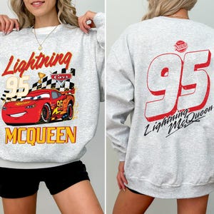 Puede incluir: Una sudadera gris claro con Lightning McQueen de la pel&iacute;cula Cars. El frente muestra a McQueen, el n&uacute;mero 95, una bandera a cuadros y las palabras "Lightning" y "McQueen". La parte trasera muestra un gran n&uacute;mero 95 rojo y "Lightning McQueen."