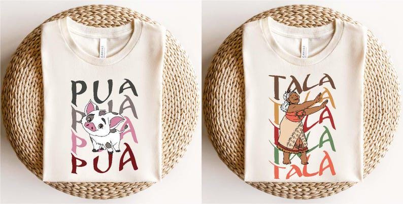 May include: Two cream-colored t-shirts with graphic designs. One features a cartoon pig with the word "PUA" in gray, pink, and maroon. The other shows a woman with the word "TALA" in brown, green, and orange. Both shirts are on a woven surface.