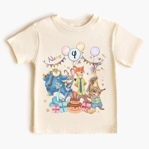 May include: Cream-colored short-sleeved t-shirt featuring a colorful cartoon illustration. The design includes characters, balloons, a birthday cake, and the number 4. The word "Name" is also visible.