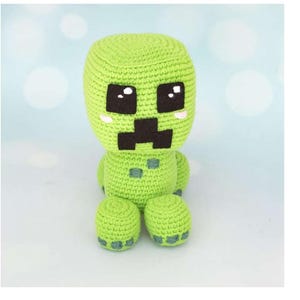 Patrón de crochet de monstruo pixelado verde, amigurumi alienígena de cabeza cuadrada en PDF, tutorial de peluche inspirado en videojuegos, descarga digital en inglés y otros términos.