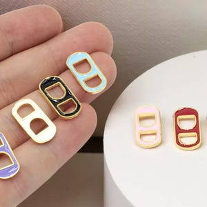 May include: A collection of colorful, enamel-coated can tab charms. The charms feature a gold-colored outline with various colors, including purple, white, black, light blue, pink, red, and yellow. These charms are ideal for jewelry making or crafting projects.