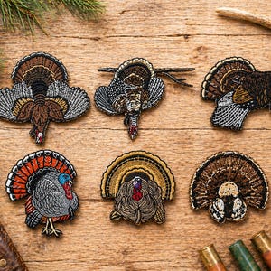 May include: Embroidered turkey patches in various poses and colors, including brown, orange, and blue. The patches are arranged on a wooden surface, showcasing detailed stitching and design. The patches are ideal for crafting or adding to clothing.