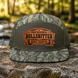 May include: A camouflage trucker hat with a brown patch that reads "PROFESSIONAL BULLSHITTER WORLD CHAMPION" in a vintage style. The hat has a mesh back and a flat brim, perfect for outdoor activities.