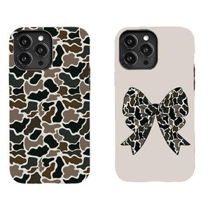 May include: Two phone cases. One features a camouflage pattern in shades of brown, black, and gray. The other case is light beige with a camouflage bow design in similar colors. Both cases have a camera cutout.