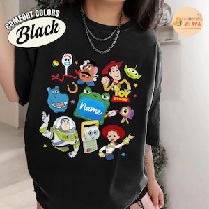 May include: Black t-shirt featuring colorful cartoon characters from the Toy Story movie. The shirt includes images of Woody, Buzz Lightyear, and other characters. The words "TOY STORY" are also visible.