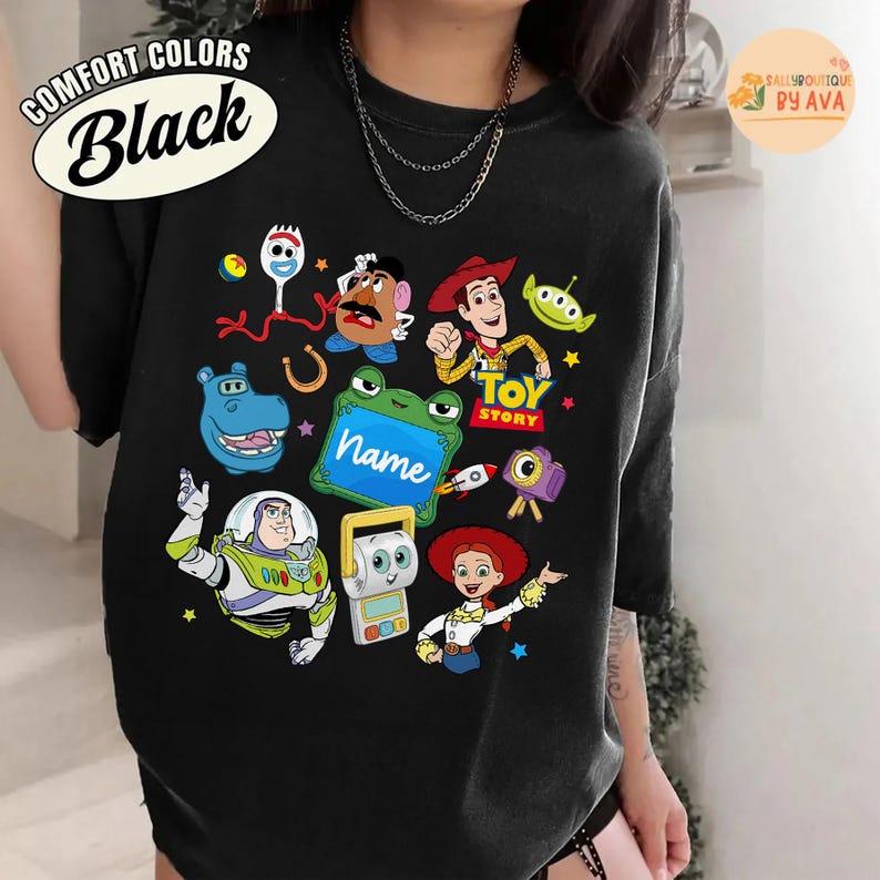 May include: Black t-shirt featuring colorful cartoon characters from the Toy Story movie. The shirt includes images of Woody, Buzz Lightyear, and other characters. The words "TOY STORY" are also visible.