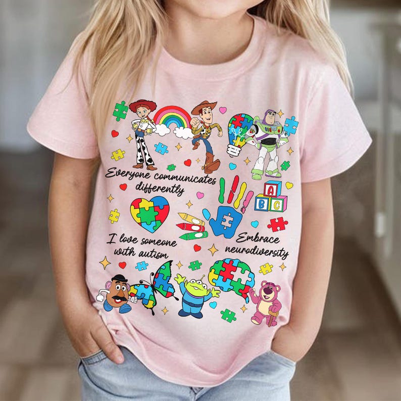 May include: Pink t-shirt featuring Toy Story characters and puzzle pieces. The shirt includes the phrases "Everyone communicates differently", "I love someone with autism", and "Embrace neurodiversity". The design incorporates a rainbow and various colorful elements.