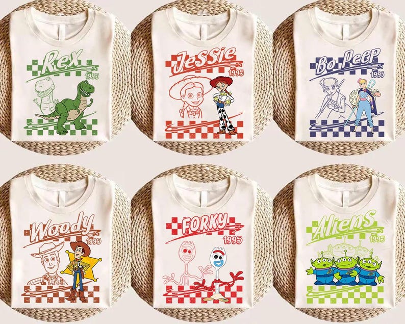 May include: Six white t-shirts featuring characters from the movie Toy Story. Each shirt has a different character design, including Rex, Jessie, Bo Peep, Woody, Forky, and Aliens, with the year 1995. The designs are set against a checkered background.