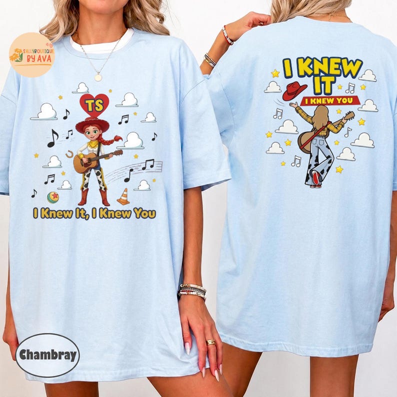 May include: A light blue t-shirt featuring a graphic of a cowgirl character playing a guitar on the front and back. The front includes the text "I Knew It, I Knew You" with musical notes, clouds, and stars. The back shows the same character with the text "I KNEW IT I KNEW YOU" and a red cowboy hat.