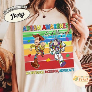 May include: Ivory-colored t-shirt with the words "AUTISM AWARENESS And Beyond!" and the phrases "ACCEPTTANCE, INCLUSION, ADVOCACY". The shirt features cartoon characters Woody and Buzz Lightyear, with puzzle piece designs.