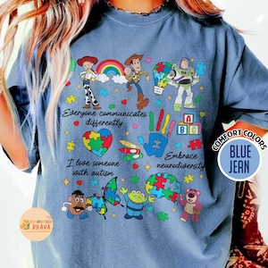 May include: Blue jean comfort colors t-shirt with a colorful graphic design. The design includes cartoon characters, puzzle pieces, and the phrases "Everyone communicates differently", "I love someone with autism", and "Embrace neurodiversity".