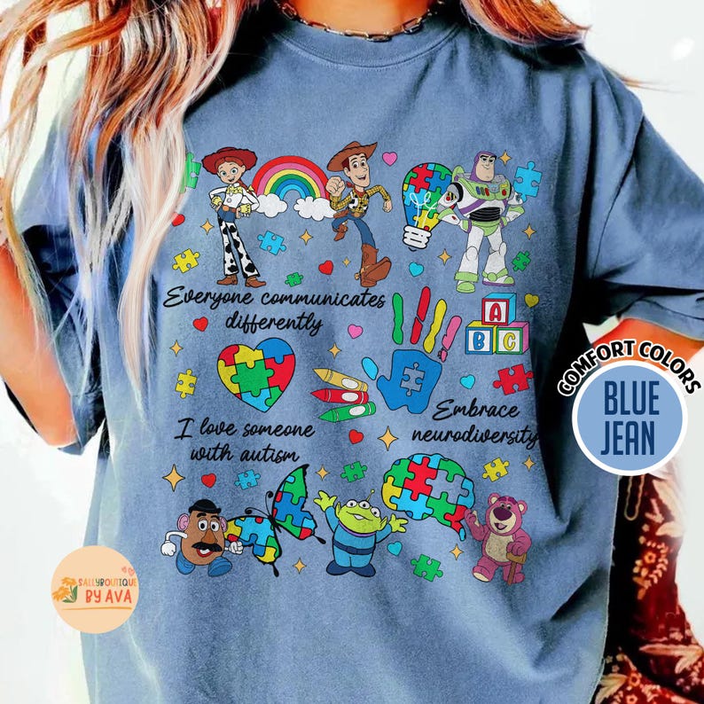 May include: Blue jean comfort colors t-shirt with a colorful graphic design. The design includes cartoon characters, puzzle pieces, and the phrases "Everyone communicates differently", "I love someone with autism", and "Embrace neurodiversity".