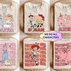 May include: Cream-colored t-shirts with colorful cartoon graphics and names. Designs include a princess, a cowgirl, and a pig, with the names "Olivia", "Susan", and "Axel". The text "We Do All Characters" is also visible.