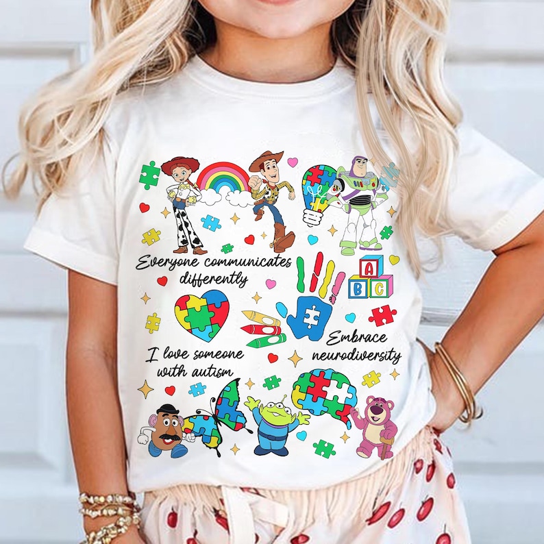 May include: White t-shirt featuring colorful cartoon characters and the text "Everyone communicates differently" and "I love someone with autism." The shirt includes a rainbow, puzzle pieces, and the phrase "Embrace neurodiversity."
