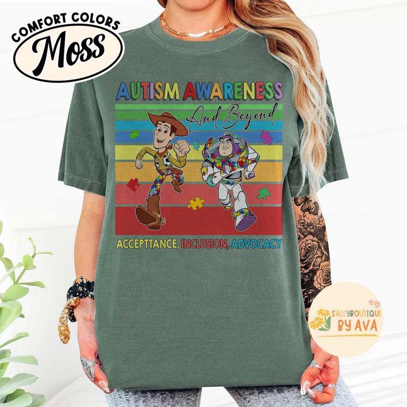 May include: Green Comfort Colors t-shirt with a graphic featuring Woody and Buzz Lightyear from Toy Story, with the text "AUTISM AWARENESS And Beyond" and "ACCEPTTANCE, INCLUSION, ADVOCACY". The shirt has a round neckline.