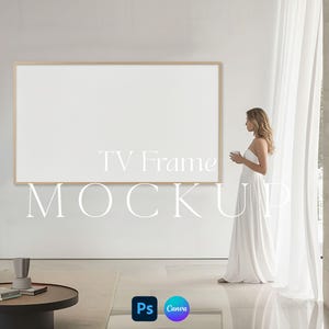 May include: A large, rectangular TV frame mockup with a light wood border is mounted on a white wall. The text "TV Frame MOCKUP" is displayed on the wall. A person in a white dress stands near a sheer curtain, holding a cup.
