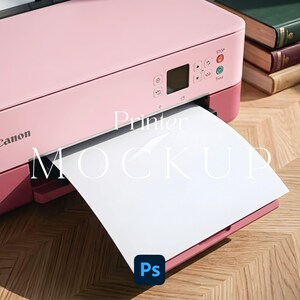 Può includere: Una stampante Canon rosa chiaro con una base rosa più scuro, dotata di schermo digitale, pulsanti di controllo e un foglio di carta bianco che fuoriesce dalla parte anteriore. Il testo Printer MOCKUP è sovrapposto in bianco e un'icona blu Ps si trova in basso.