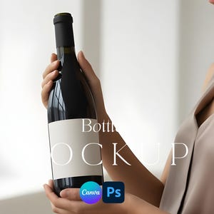 May include: A dark wine bottle with a blank white label is held by a person. The bottle has a black top and is held in front of a soft, neutral background. The text "Bottle Mockup" is visible on the bottle.