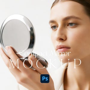May include: A close-up of a silver compact mirror held in a hand. The mirror is round and reflective. The text "Compact Mirror MOCKUP" is displayed in white. The background is a plain, neutral colour.