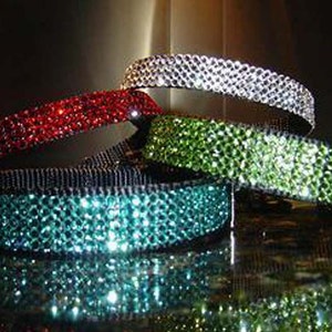 May include: Four sparkly dog collars in different colors. The collars are made of rhinestones and are arranged in a stack. The colors are red, green, teal, and silver.