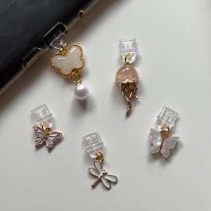 Peut inclure: Plusieurs breloques décoratives avec des motifs de papillons, de libellules et de méduses. Les breloques sont dorées, blanches et roses, avec des perles et des détails transparents. Petites et délicates, elles conviennent aux bijoux ou accessoires.