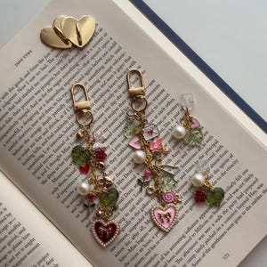 Könnte beinhalten: Goldene herzförmige Ohrring-Anhänger und zwei Paar baumelnde Ohrringe mit Herz-, Perlen- und Blumen-Anhängern. Die Ohrringe haben eine romantische, Vintage-Ästhetik und sind perfekt für einen Hauch von Eleganz.